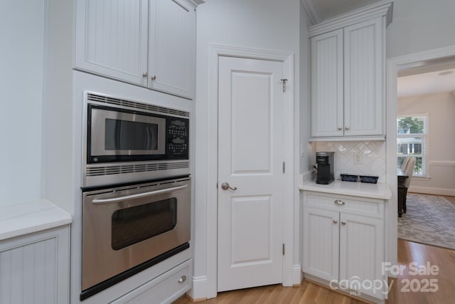 kitchen with light wood-style flooring, backsplash, light stone countertops, and stainless steel appliances