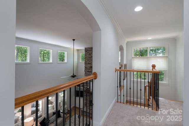 corridor featuring crown molding, arched walkways, a wealth of natural light, and an upstairs landing