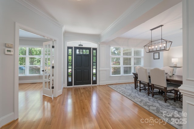 entryway featuring crown molding, a chandelier, plenty of natural light, and light wood-style flooring