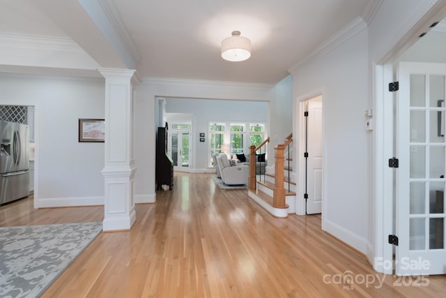 entrance foyer featuring ornamental molding, decorative columns, baseboards, stairway, and light wood finished floors
