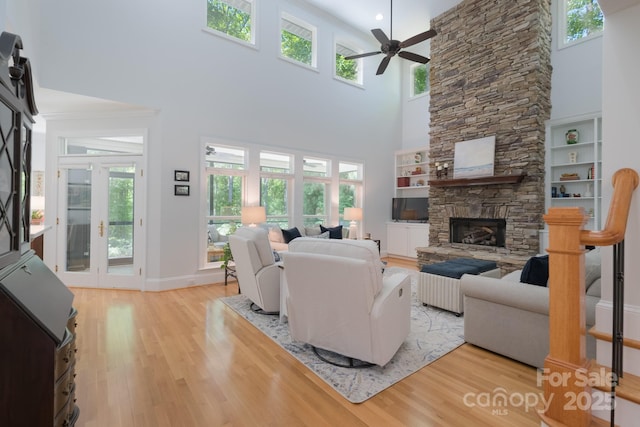 living room with light wood-type flooring, a ceiling fan, a towering ceiling, and a fireplace