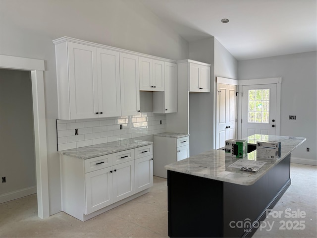 kitchen with a kitchen island, light stone countertops, baseboards, white cabinetry, and tasteful backsplash