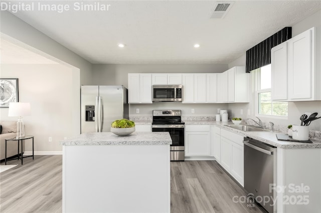 kitchen with a kitchen island, visible vents, appliances with stainless steel finishes, light wood finished floors, and a sink