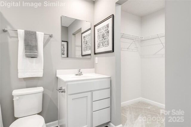 bathroom with toilet, vanity, baseboards, and a walk in closet