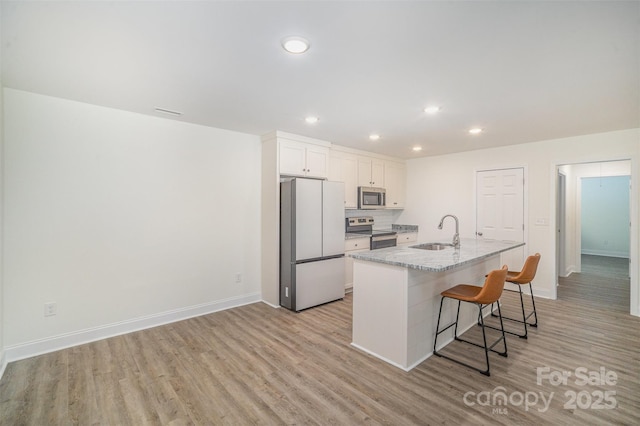 kitchen featuring light wood-type flooring, appliances with stainless steel finishes, a center island with sink, and a sink
