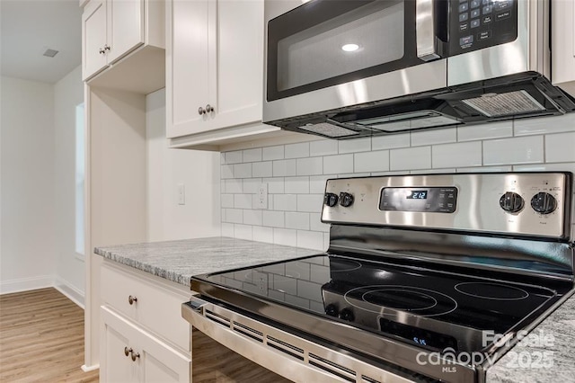 kitchen with white cabinets, stainless steel appliances, light wood-style flooring, decorative backsplash, and light stone counters