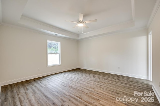 empty room with wood finished floors, a tray ceiling, and ornamental molding