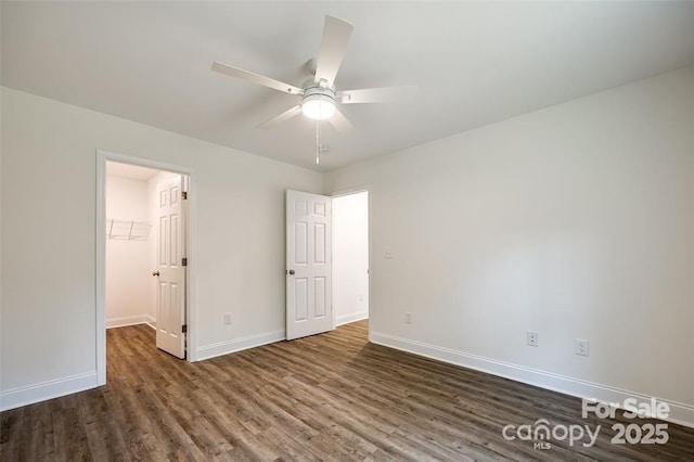 unfurnished bedroom featuring dark wood-style flooring, baseboards, a ceiling fan, a closet, and a walk in closet