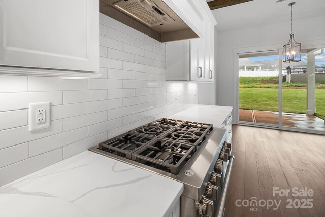 6712 Cove Ln, Sherrills Ford, NC 28673 - kitchen with stainless steel gas range, ventilation hood, a chandelier, decorative backsplash, and white cabinetry