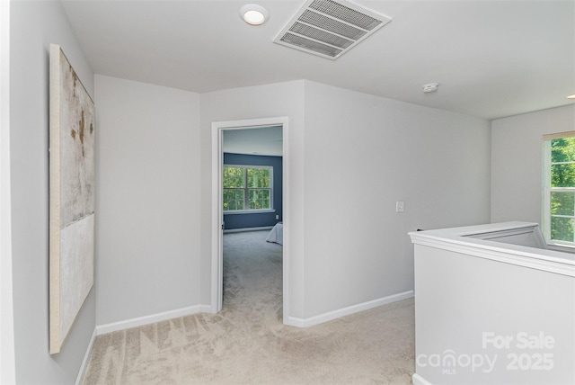 hallway with visible vents, baseboards, and light carpet