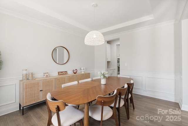 dining area featuring wood finished floors, a decorative wall, a wainscoted wall, and a tray ceiling