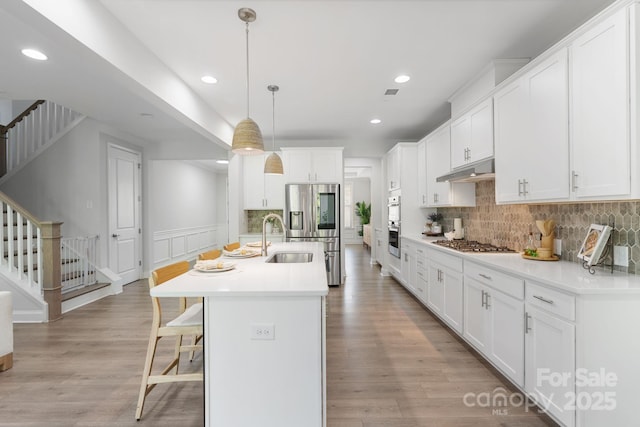 kitchen with decorative backsplash, a sink, stainless steel appliances, under cabinet range hood, and a kitchen island with sink