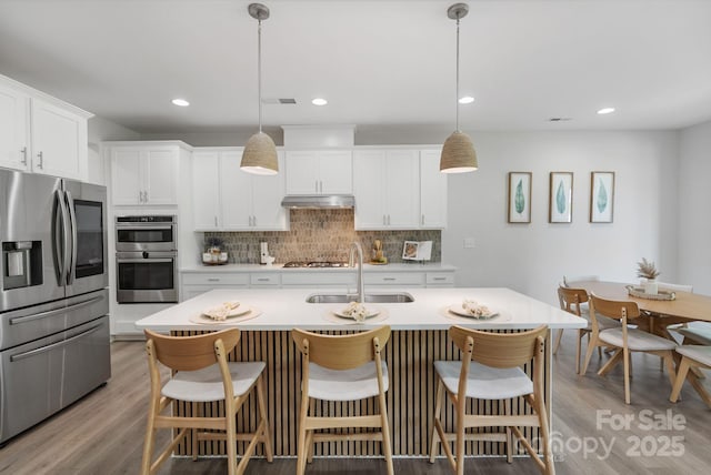kitchen featuring a sink, backsplash, stainless steel appliances, and light wood-type flooring