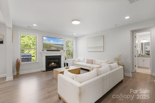living area featuring recessed lighting, a fireplace with flush hearth, wood finished floors, and baseboards