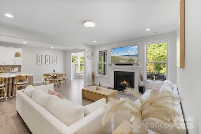 living room with visible vents, recessed lighting, a fireplace with flush hearth, and light wood finished floors