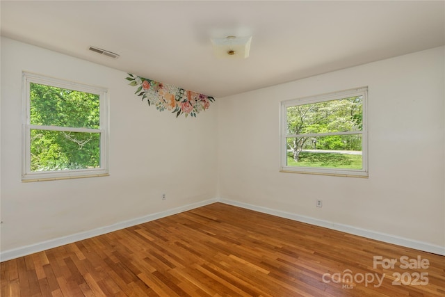 empty room with baseboards, visible vents, wood finished floors, and a wealth of natural light