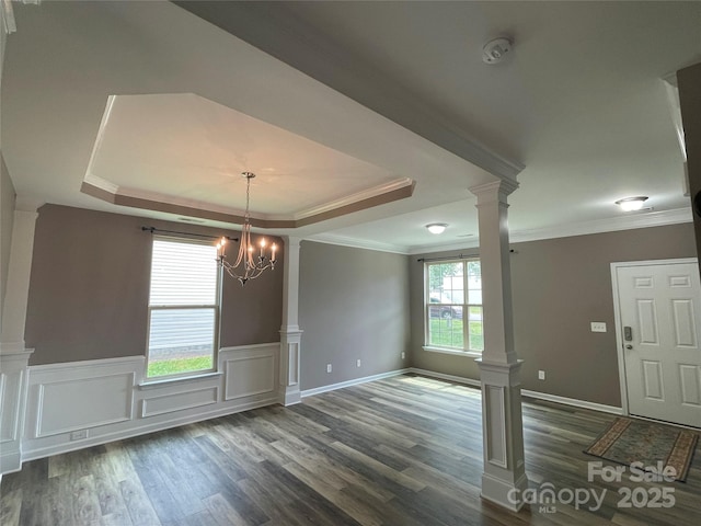 unfurnished dining area with a raised ceiling, dark wood-style floors, ornamental molding, ornate columns, and wainscoting