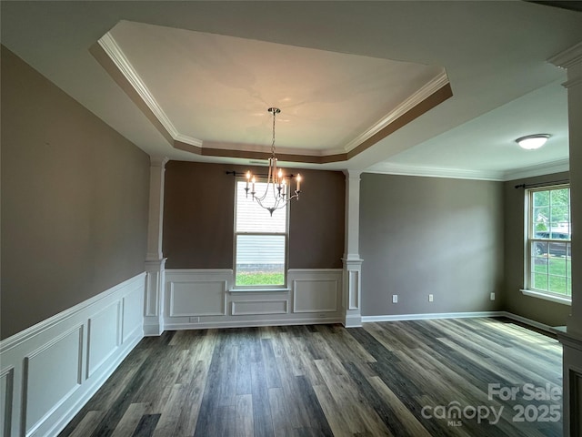 unfurnished dining area featuring a decorative wall, a chandelier, ornamental molding, dark wood-type flooring, and a tray ceiling