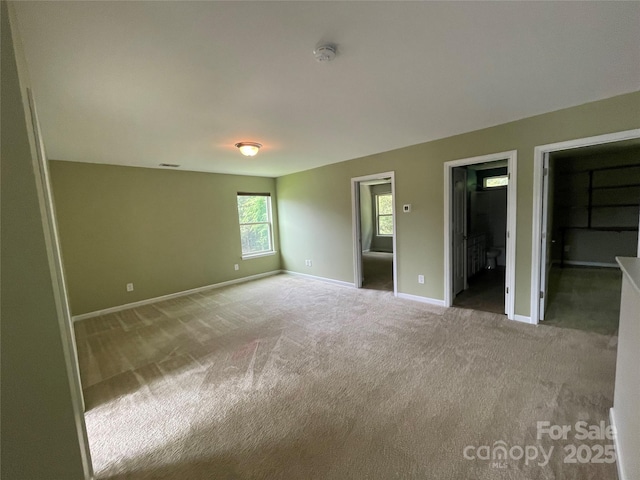unfurnished bedroom featuring connected bathroom, a spacious closet, carpet floors, and baseboards