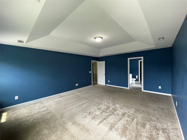 spare room featuring carpet floors, visible vents, a tray ceiling, and baseboards