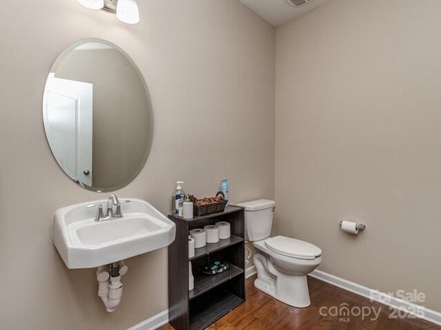 half bath with a sink, toilet, wood finished floors, and baseboards
