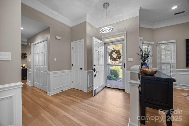 foyer featuring light wood-style floors, a decorative wall, crown molding, and wainscoting