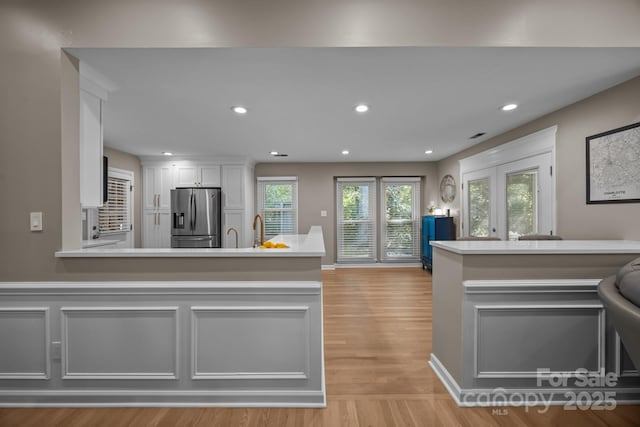 kitchen featuring stainless steel refrigerator with ice dispenser, light countertops, white cabinets, a peninsula, and light wood-style floors