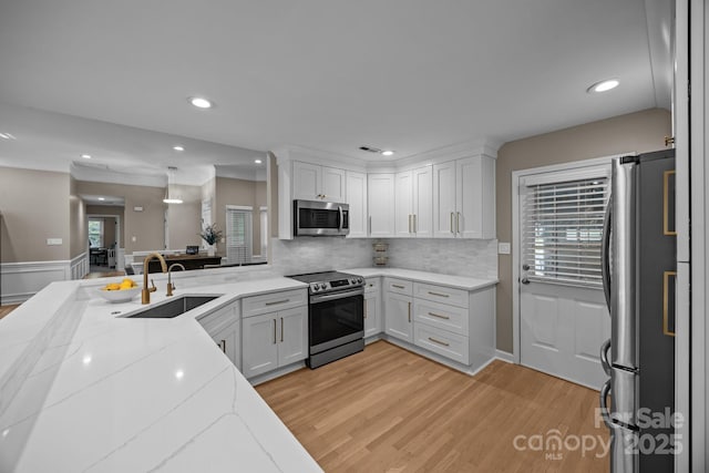 kitchen featuring white cabinets, light stone counters, a sink, stainless steel appliances, and light wood-type flooring