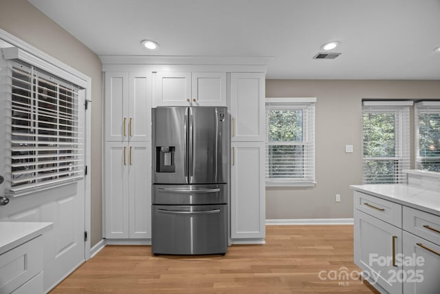 kitchen featuring stainless steel refrigerator with ice dispenser, light wood-style flooring, baseboards, and visible vents