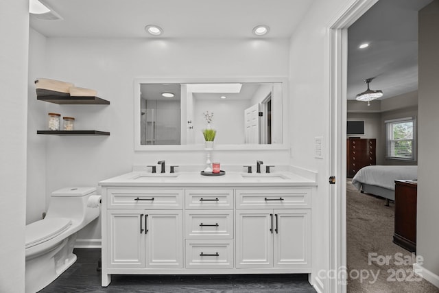 ensuite bathroom featuring double vanity, toilet, baseboards, and a sink