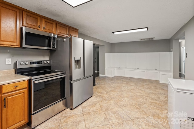 kitchen featuring light tile patterned floors, stainless steel appliances, brown cabinetry, visible vents, and light countertops