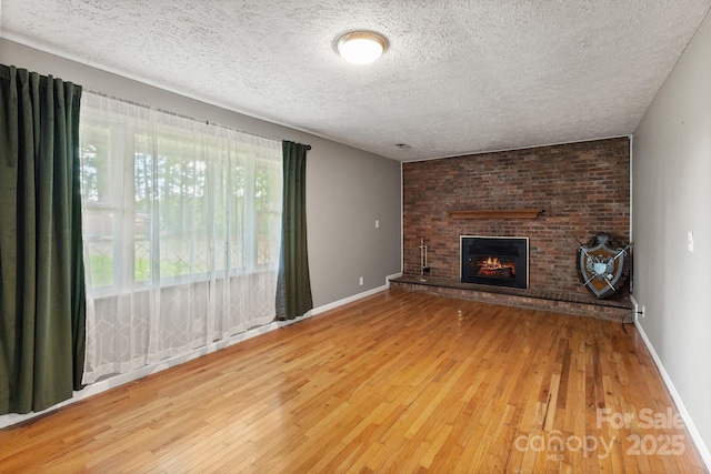 unfurnished living room featuring a textured ceiling, a brick fireplace, baseboards, and hardwood / wood-style floors
