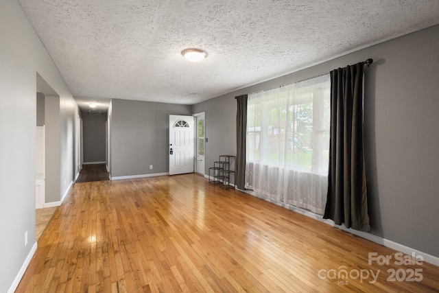 interior space with light wood finished floors, a textured ceiling, and baseboards