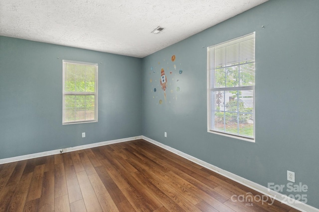 empty room with dark wood-style flooring, a textured ceiling, baseboards, and visible vents