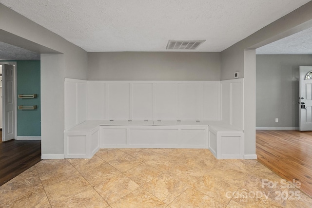 empty room featuring light wood finished floors, a textured ceiling, visible vents, and baseboards
