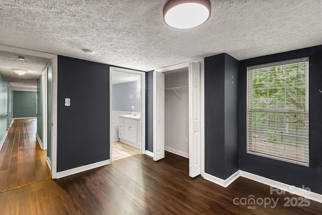 unfurnished bedroom with a textured ceiling, baseboards, and wood finished floors