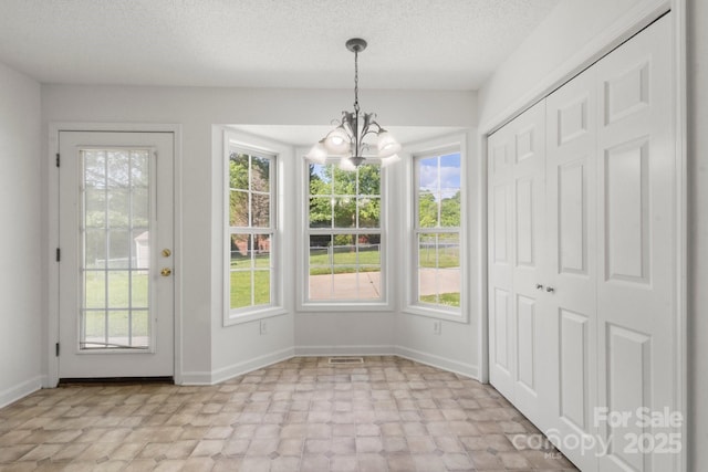 unfurnished dining area with an inviting chandelier, a textured ceiling, baseboards, and visible vents