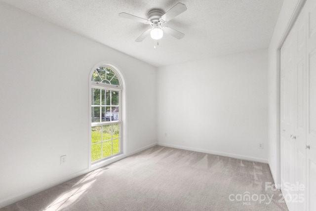 empty room featuring a textured ceiling, ceiling fan, light colored carpet, and baseboards