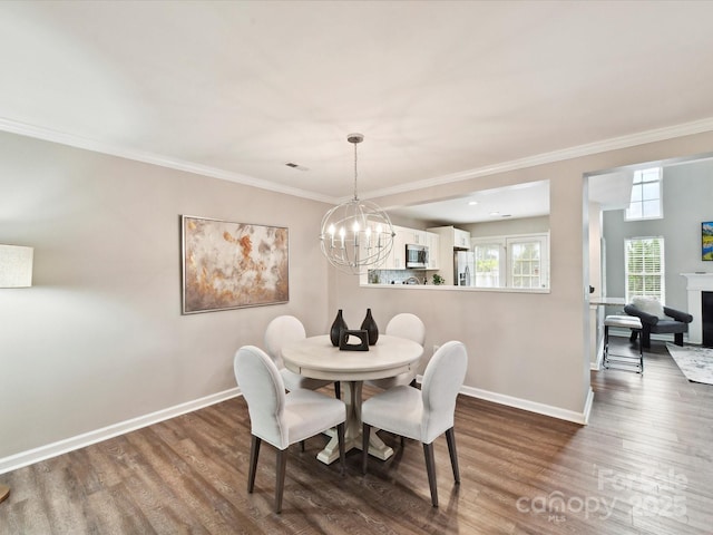 dining space featuring baseboards, wood finished floors, a chandelier, crown molding, and a fireplace