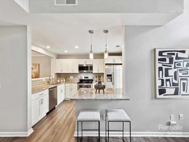 kitchen featuring stainless steel appliances, a sink, decorative backsplash, white cabinetry, and wood finished floors