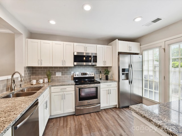 kitchen featuring appliances with stainless steel finishes, a sink, white cabinetry, light wood finished floors, and decorative backsplash