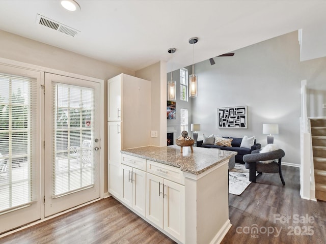 kitchen featuring a peninsula, wood finished floors, white cabinets, decorative light fixtures, and light stone countertops