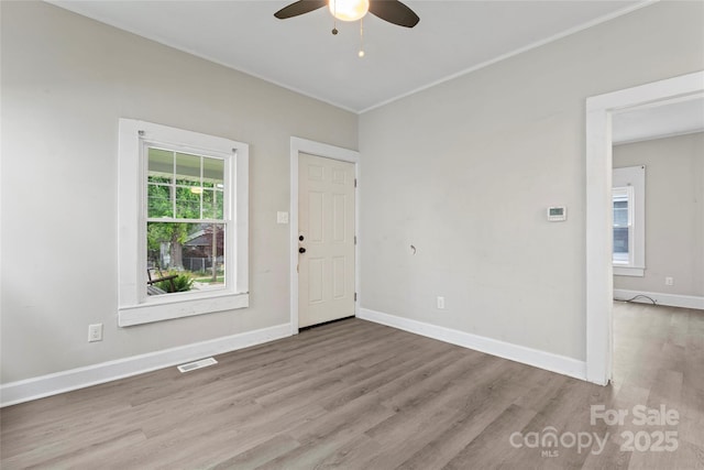 empty room featuring a ceiling fan, visible vents, baseboards, ornamental molding, and wood finished floors