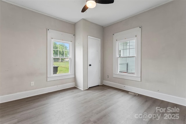 empty room featuring a ceiling fan, visible vents, wood finished floors, and baseboards