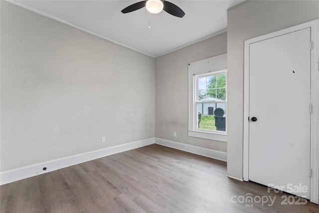 empty room with wood finished floors, ceiling fan, crown molding, and baseboards