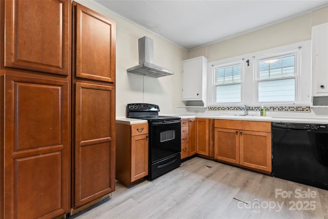 kitchen with light wood-style flooring, light countertops, wall chimney range hood, black appliances, and a sink