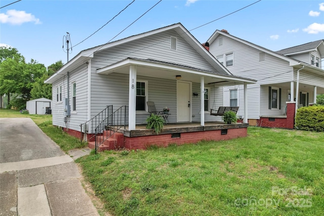 bungalow-style house featuring an outbuilding, a storage shed, covered porch, crawl space, and a front lawn