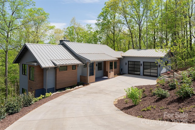 view of front of property with a standing seam roof, a chimney, driveway, metal roof, and a garage