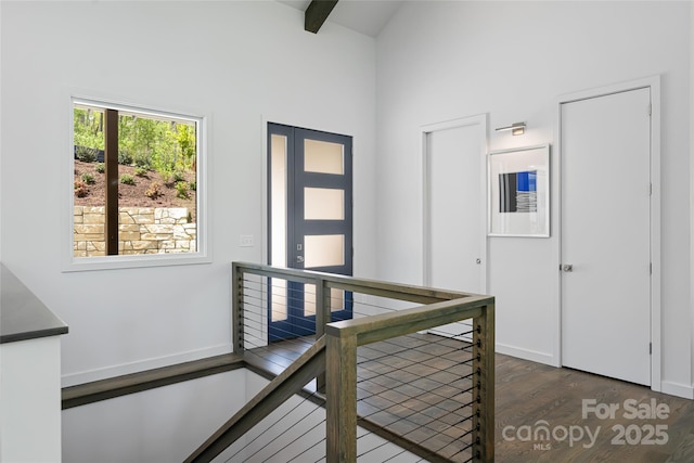 hall featuring a towering ceiling, wood finished floors, baseboards, beamed ceiling, and an upstairs landing