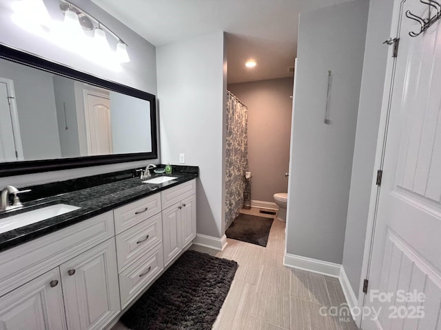 bathroom featuring a sink, double vanity, toilet, and baseboards